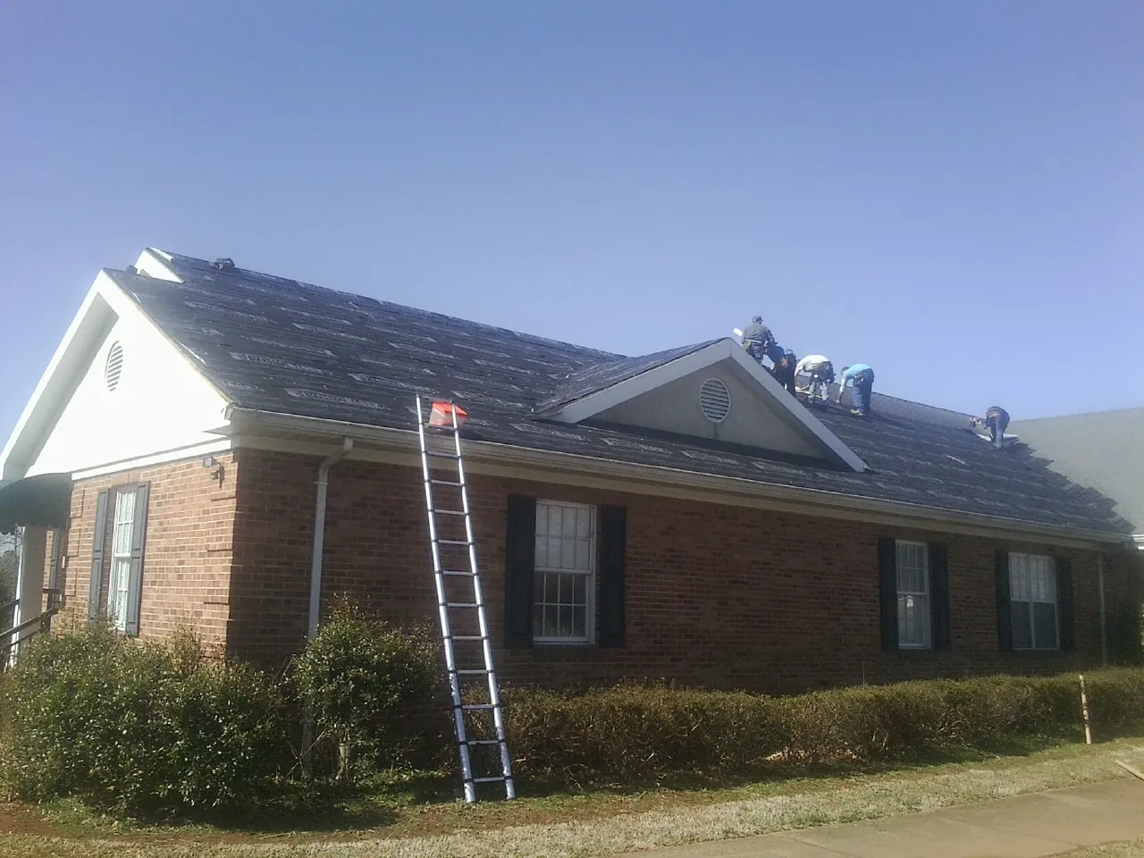 Crew tearing shingles off a brick ranch roof with a ladder set — Metal Roof Repair work by our crew in West Barnstable