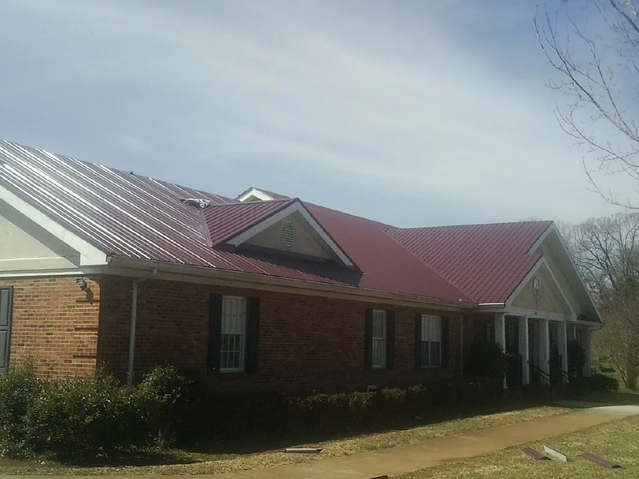 Red metal roof with gabled entries on a long brick building, from a Hail Damage Roof Repair job in West Barnstable