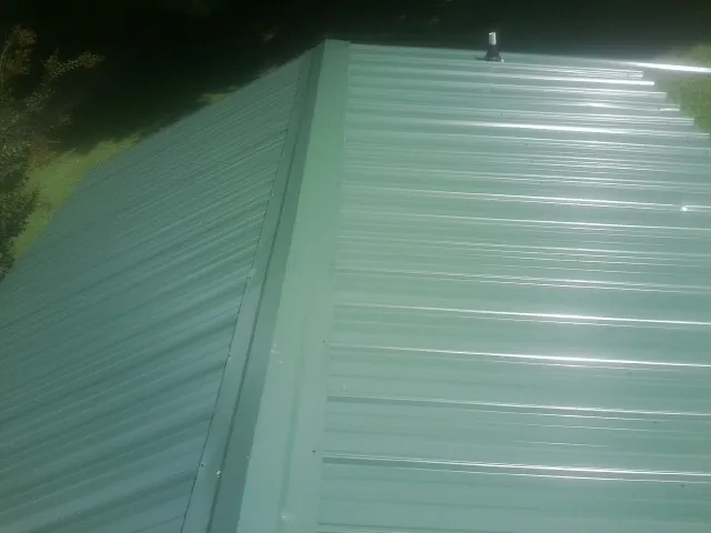 New green metal panels meeting at the ridge of a roof — Flat Roof Repair work by our crew in West Barnstable