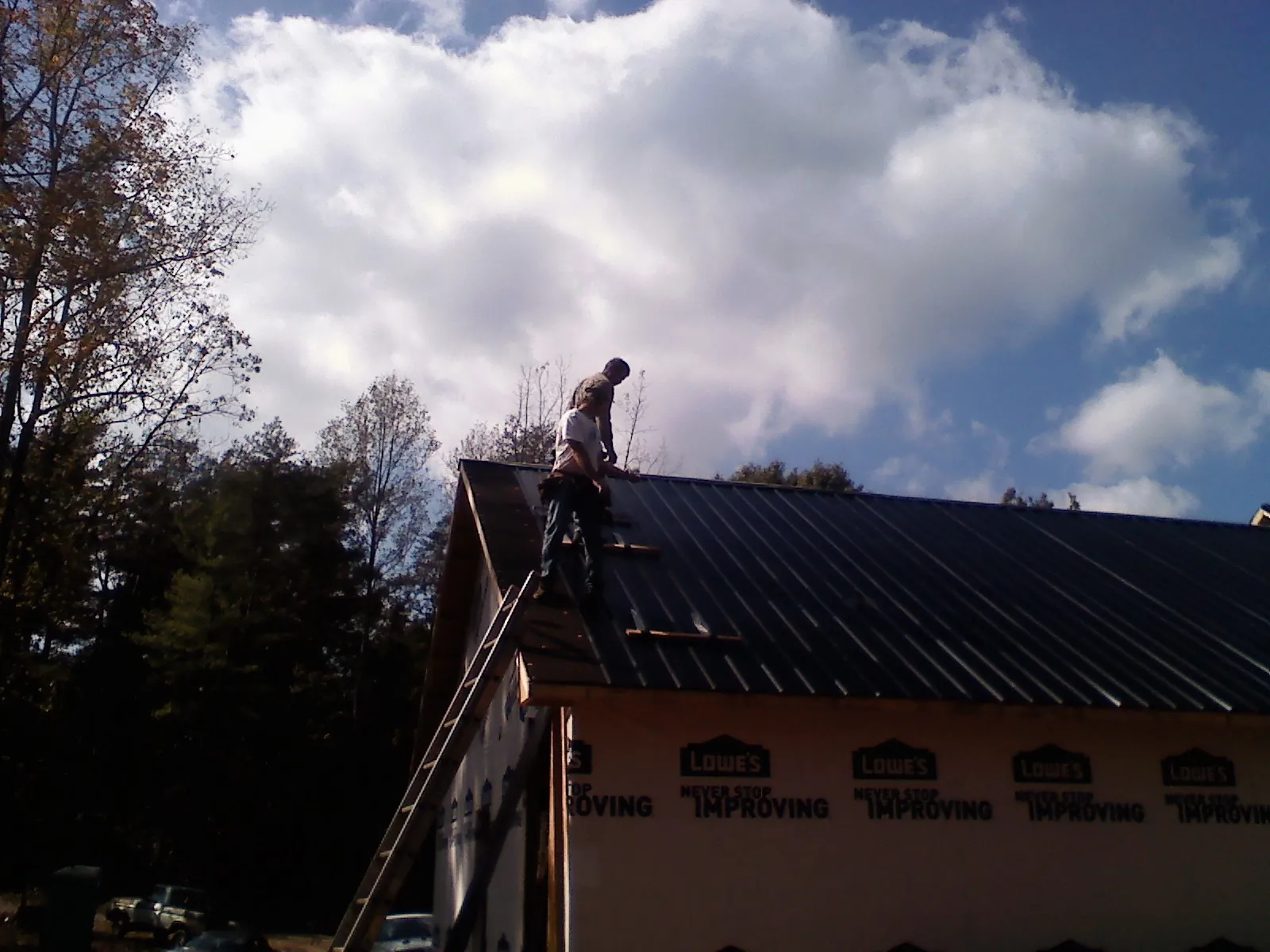 Roofer fastening dark metal panels high against a cloudy sky, from a Roof Inspection job in West Barnstable