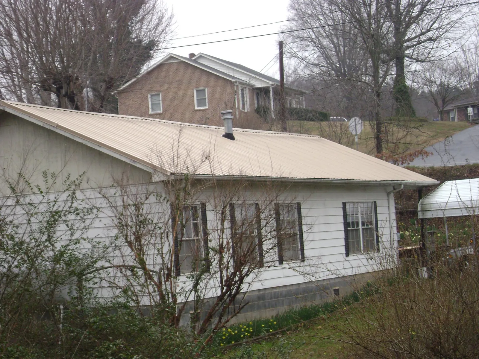 Tan metal roof on a white sided house set into a hillside — Commercial Roofing by Roofing Brothers in West Barnstable